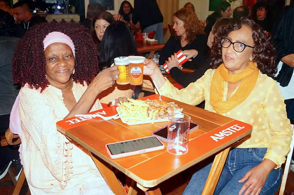 Duas mulheres brindando com chope em uma mesa de boteco