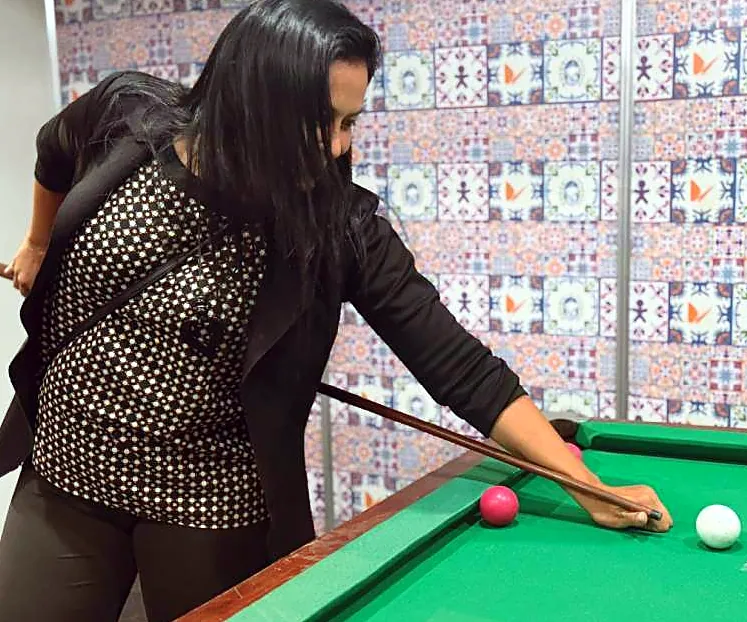 Mulher jogando sinuca diante de um painel de azulejos